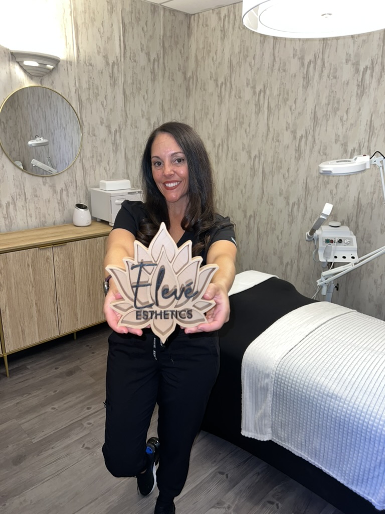 Esthetician Dina Abril holding the Elevé Esthetics sign in her studio