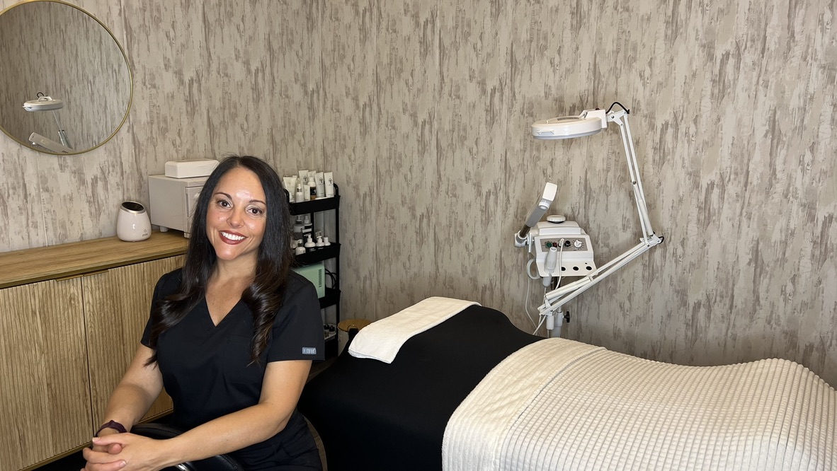 Esthetician Dina Abril seated beside the facial treatment bed in her studio